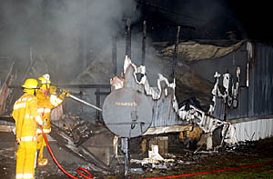 Two Troy firemen douse the smoldering remains of a mobile home at 630 Harrison St. early Saturday.