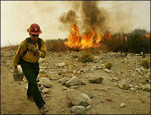 A firefighter walks by the wildfires that threaten the Rancho Cucamonga, California area on Firday 24 October, 2003. Wildfires in the area have burnt thousands of acres of forests and forced evacutation of homes in the area.
