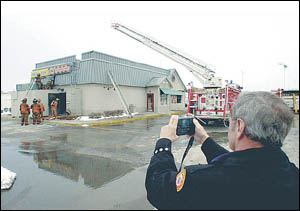 As firefighters search for fire in the roof, Jerry Quick, an Independence fire inspector, takes a photograph of the damage from a fire in a Long John Silvers restaurant at 39th Street and M291 Wednesday morning.