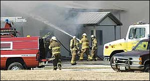 Firefighters train a stream of water through a cloud of dark smoke Wednesday afternoon at the Bronc Busters Restaurant and Lounge on Highway 59, about four miles north of Diamond. A Carthage firefighter was killed while battling the blaze from inside the metal building.
