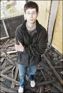 Charles Sotiriou, 14, yesterday stands amid the charred remains of the porch where the Staten Island fire broke out.