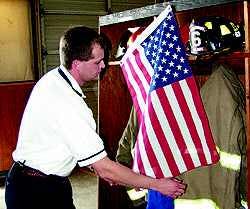 Vann&apos;s Crossroads Fire Chief Jamey Jones hangs a flag over Phillip Hulen&apos;s turn out gear on Wednesday