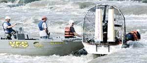 Grand Forks fire/rescue training officers Dave Manthei, (right) leans over to attach a rope to a rivercraft that is stuck on rocks.