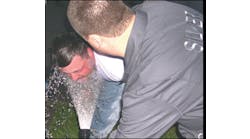 An OC pepper spray victim is rinsed with cool water from a garden hose. He will then be directed to dry himself with a clean cloth and report to paramedics for an evaluation.
