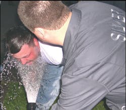 An OC pepper spray victim is rinsed with cool water from a garden hose. He will then be directed to dry himself with a clean cloth and report to paramedics for an evaluation.