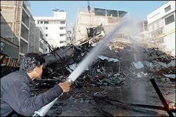 A Thai firefighter sprays water to smoldering debris as his fellow firefighters are trapped inside the collapsed building in Bangkok, Thailand, on Monday, Jan. 10, 2005. The six-story building collapsed in the Thai capital Sunday about two hours after it caught fire, trapping about five firefighters inside the wreckage, police said.