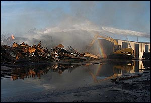 Firefighters shoot water into the burned part of a Kropf Lumberyard warehouse as a back hoe pulls out burning wood in Hesston, Kan., Wednesday afternoon, Jan. 26, 2005. The early morning blaze destroyed hundreds of thousands of dollars of building material inventory. Firefighters from Hesston, Newton and Moundridge, Kan., contained the fire but the large amount of wood in the metal structure continued to burn and smolder.