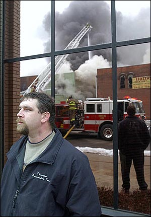 Ron Schweitzer watches firefighters work to put out a fire in Dover, Ohio with the scene reflected behind him, Thursday, Feb. 3, 2005. The fire damaged an entire city block.