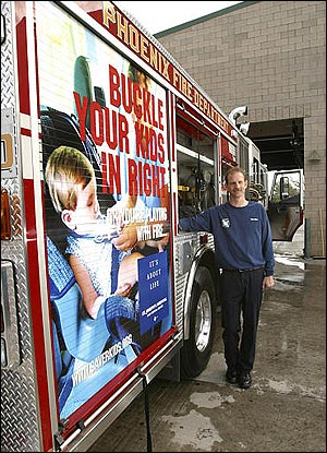 Phoenix Fire Captain Tony Mure of Station 30 shows off an ad on a fire engine in Phoenix, Ariz.. Wednesday, Feb. 16, 2005. Phoenix firefighters have turned 10 of their trucks into rolling billboards, carrying public-safety messages about watching children around water and buckling up.