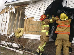 Stansburg volunteer firefighters cover a broken window after several mobile homes received damage from strong winds in Wilson, N.C., Tuesday, March 8, 2005. No one was injured but several people have been evacuated to area hotels as officials deemed their homes unsuitable for habitation.