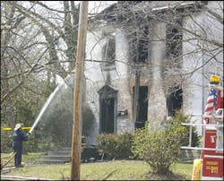 A firefighter sprays water into a window of a house where a fire killed three people and injured two others, near the campus of Miami University, Sunday, April 10, 2005 in Oxford, Ohio