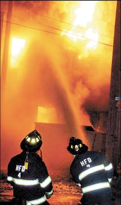 Two firefighters operate a ground monitor at the rear of the building.