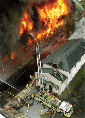 The collapse zone has been cleared. Master streams operate on the fire building as firefighters protect a vacant exposure across the street.