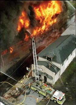 The collapse zone has been cleared. Master streams operate on the fire building as firefighters protect a vacant exposure across the street.