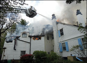 Firefighters in Port Washington&rsquo;s tower ladder utilize their deluge guns to knock down fire in the exposure 4 side of the building, above the garage (lower left), where the fire is believed to have started. The photo shows the exposure 3-4 side.