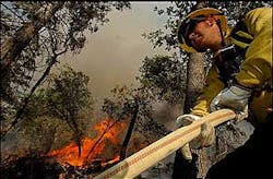 U.S. Forest Service Firefighter Michael Hoon pulls hose while fighting a wildfire in the Barton Flat area of the San Bernardino National Forest, Calif., Tuesday, July 5, 2005.