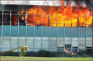 A firefighter drags hose across the grass as flames pour out the windows of Wasatch Junior High School in Salt Lake City, on Monday, July 11, 2005.