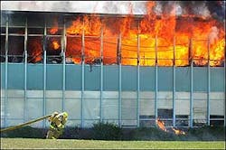 A firefighter drags hose across the grass as flames pour out the windows of Wasatch Junior High School in Salt Lake City, on Monday, July 11, 2005.