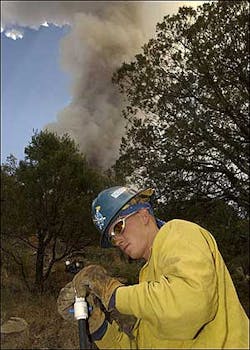 Smoke billows into the air from the Florida Fire as Northwest Fire District firefighter Tyler Roberts adjusts a sprinkler head while in Madera Canyon outside Tucson, Ariz., during structure protection of the buildings, Tuesday, July 12, 2005.
