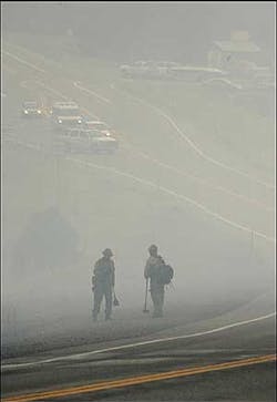 Two firefighters stand along Colorado 160 waiting for air drops as police stop cars because of a forest fire west of Pagosa Springs, Colo., Saturday, July 16, 2005. Traffic along Colorado 160 was stopped for a time in order to let an air tanker make fire retardant drops.