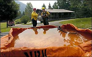 Tom McIsaac, left, and Brant Waldron, both with the Frenchtown Fire department, talk structure protection, behind a portable water supply, at a home on West Mountain Road near Alberton, Mont., as a wildfire burns nearby Monday, Aug. 8, 2005.