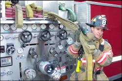 A lone firefighter pulls the bundled line with one hand while the other hand supports the bundle as it slides out of the bed.