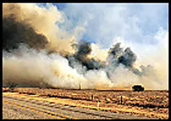 Smoke from a large brush fire and burning debris billows across FM 171 Wednesday between Wichita Falls and Charlie. A firefighter injured in the blaze remains in critical condition with second-degree burns.