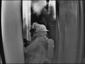 Photo 3. Firefighters enter a compartment on a ship. The push of heat into the hallway indicates they have fire inside the compartment. The wall in the hallway is hotter on the left than on the right, helping firefighters identify the fire room.