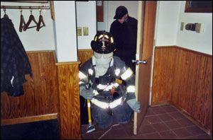 Using the protective hood backwards, a firefighter starts searching a room. The firefighter in the background was unable to take part in the drill, but was used to help members move through the course.