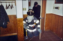 Using the protective hood backwards, a firefighter starts searching a room. The firefighter in the background was unable to take part in the drill, but was used to help members move through the course. Using the protective hood backwards, a firefighter starts searching a room. The firefighter in the background was unable to take part in the drill, but was used to help members move through the course.