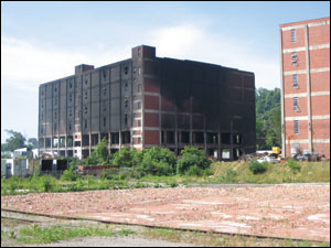 The northeast corner of the warehouse after the fire was extinguished. The brick walls were knocked out of the first two floors of the building to allow water application to the burning materials. The third through the sixth floors were empty. Shredded plastic material was stored in four-by-four-by-four-foot boxes stacked three high on pallets. The warehouse to the right was of identical construction and used for storage of shredded plastic. This warehouse was full on all six floors.