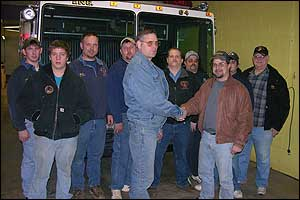 Niles English, President of Laceyville's Good Will Fire Company, front left, shakes hands with Chris Kemmerling, President of the Clover Volunteer Fire Company in Schuylkill County Wednesday night when Laceyville donated its 1987 KME pumper (seen behind the group) to Clover.
