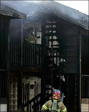 As one firefighter keeps watch, another walks along a second-floor balcony of the apartment complex.