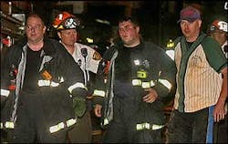Emergency medical workers and fellow firefighters escort an injured firefighter to a waiting ambulance at a four-alarm fire. Emergency medical workers and fellow firefighters escort an injured firefighter to a waiting ambulance at a four-alarm fire.