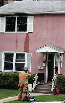 A firefighter removes his gear after exiting the building. The second floor window is what blew out as crews entered the structure.