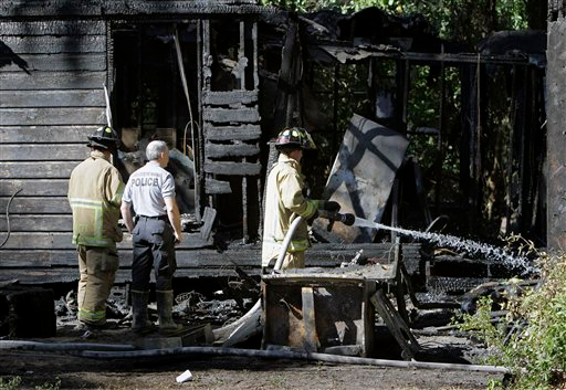 An official from the Florida State Fire Marshall's office, center, watches as members of Marion County Fire Rescue douse hot spots at the scene of a house fire that killed five children.