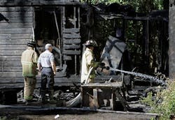 An official from the Florida State Fire Marshall&apos;s office, center, watches as members of Marion County Fire Rescue douse hot spots at the scene of a house fire that killed five children.
