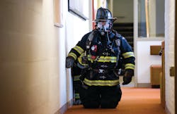 A Worcester firefighter prepares to lead a search-and-rescue team into a classroom building, guided by incident command testing a locator/tracking device.