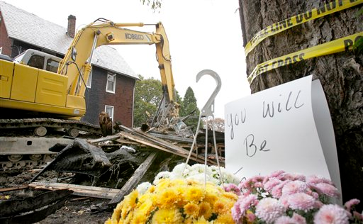 A basket of flowers and a note are seen under a tree nearby as a demolition crew removes the debris from a home where two people died on Oct. 21.