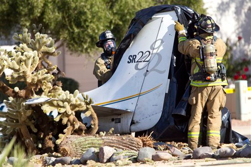 Firefighters remove a tarp from the remains of a small aircraft that crashed in the front yard of a northeast Phoenix home.