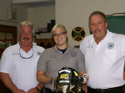 Battalion Chief Nick Devita, Brandi DuCoeur and Fire Chief James Ganter, with Brandi displaying her fire helmet and badge.