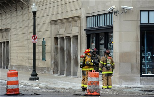 Firefighters talk near construction barrels that mark an open manhole and debris in front of Orchestra Hall on Feb. 12.