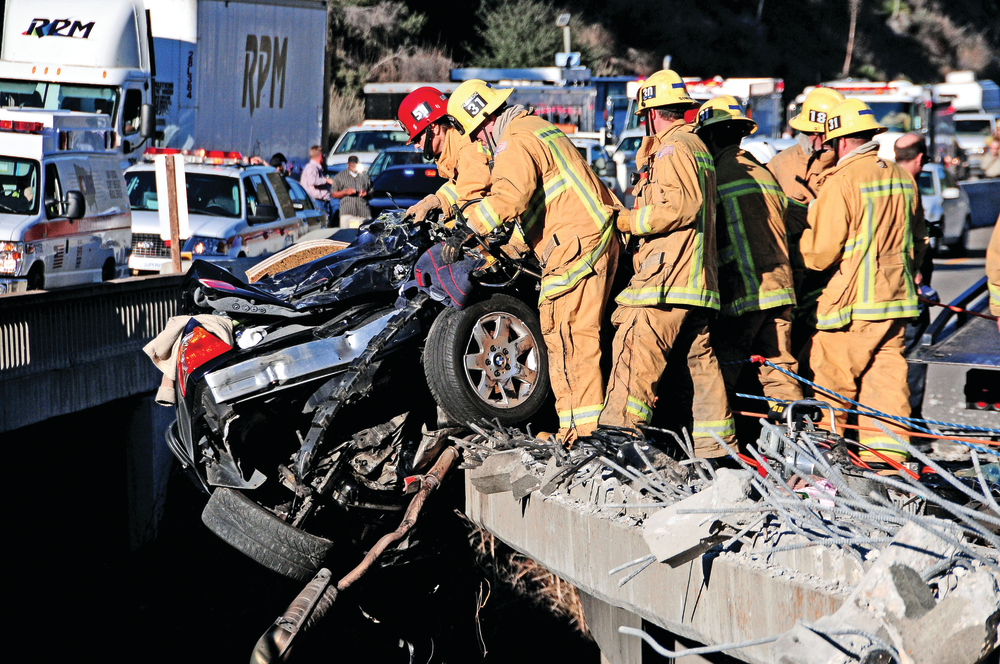 Upon arrival of the first units, a tractor-trailer truck had rear-ended a car. The truck dragged the car under its wheels and crashed through the bridge. Landing 100 feet below, the truck caught fire and the car was hanging off the highway directly above.