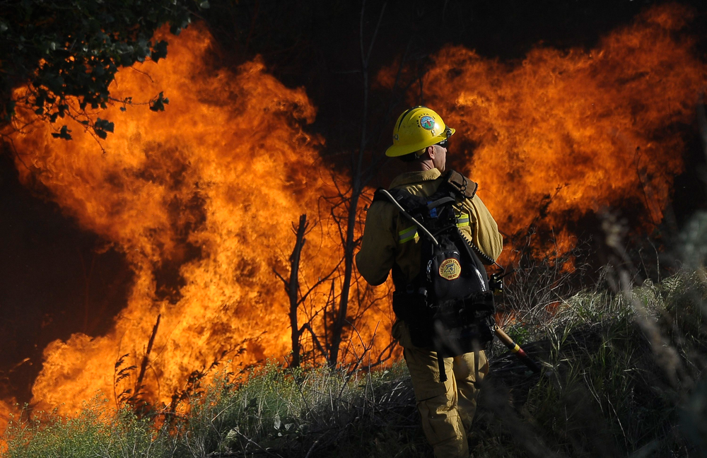 A Los Angeles County firefighter battles a wall of fire, a result of a brush fire, in Acton on May 8.