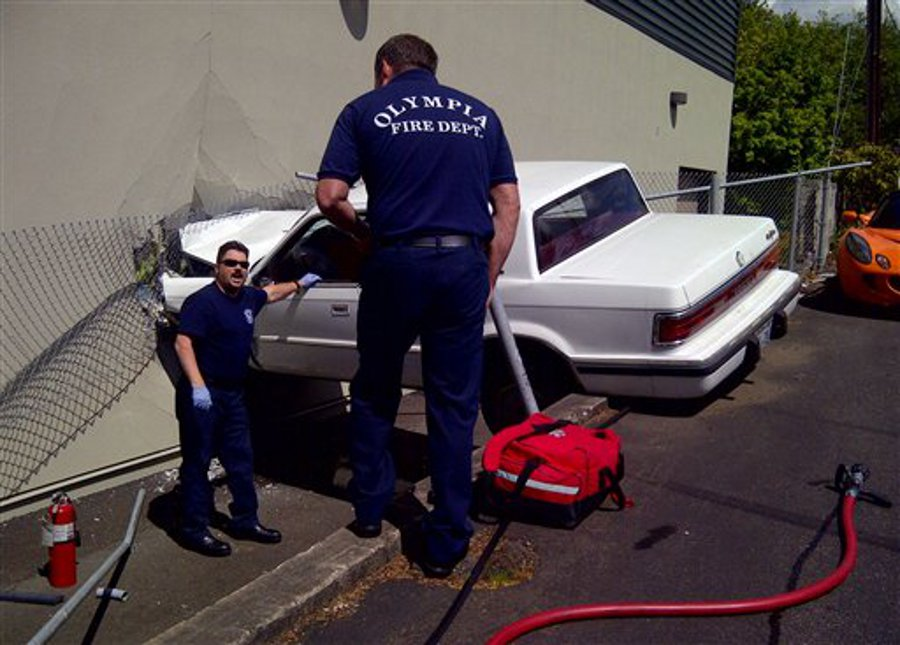 Firefighters discuss how to remove a man from a car after he crashed it into TVW Studios in Olympia, Wash. on May 9.