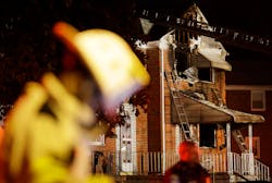Officials stand in front of a fire-damaged house in Baltimore, where an early morning fire claimed the lives of an adult and four children on Oct. 11.