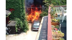 A photo taken from a video shows side C of the fire building prior to the fire department&apos;s arrival. The outside deck area is on fire and flames are spreading to a car and the interior of the building through first-floor windows.