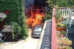 A photo taken from a video shows side C of the fire building prior to the fire department's arrival. The outside deck area is on fire and flames are spreading to a car and the interior of the building through first-floor windows. A photo taken from a video shows side C of the fire building prior to the fire department's arrival. The outside deck area is on fire and flames are spreading to a car and the interior of the building through first-floor windows.