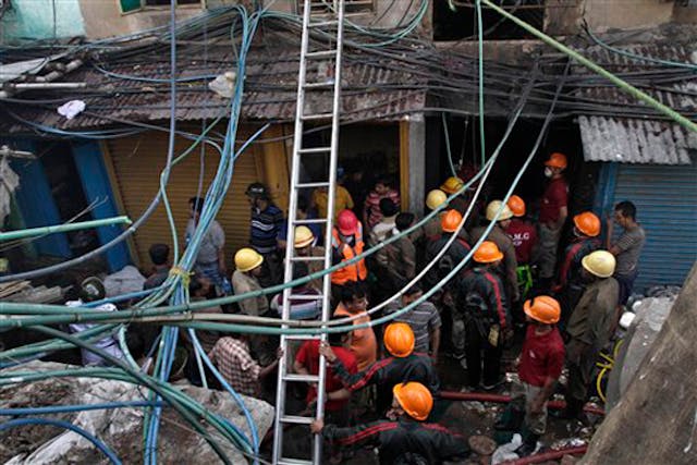 Firemen and rescuers wait outside an illegal six-story plastics market where a fire broke out early in the morning in Kolkata, India, Wednesday, Feb. 27, 2013. The fire was under control but toxic gases being released by the blaze were hampering rescue efforts. More than a dozen people were killed and others were hospitalized in critical condition.