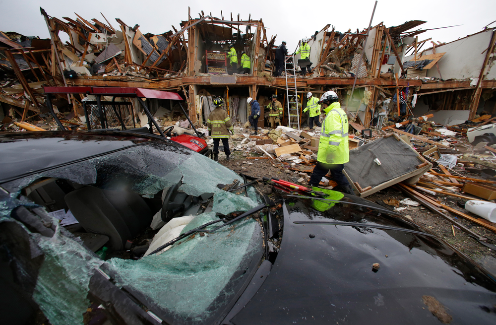 A smashed car sits in front of an apartment complex that was destroyed by the explosion in West, Texas, as firefighters conduct a search and rescue Thursday.